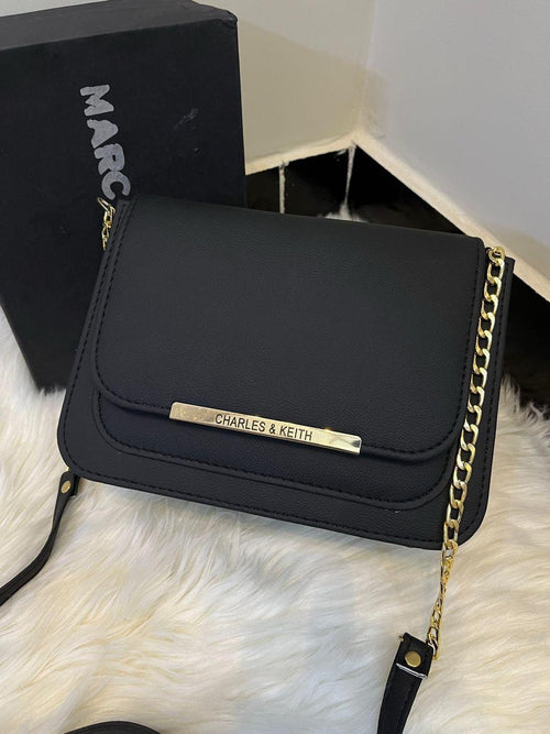 Black handbag with gold chain strap on a white fur surface, with 'Marc' visible in the background.