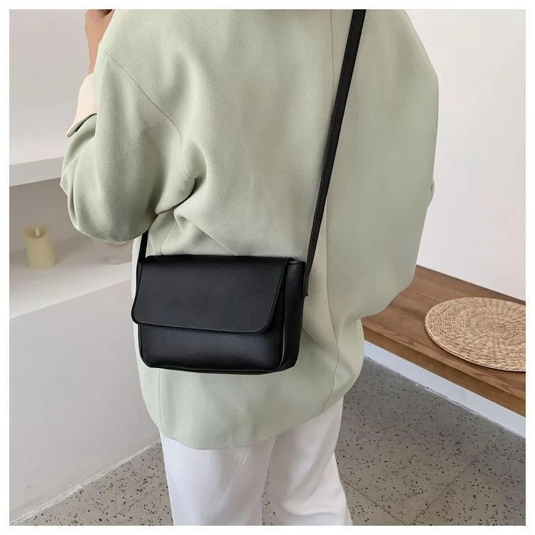 Person wearing a light green sweatshirt with a black crossbody bag in an indoor setting.