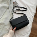 Black handbag held by a person on a light-colored fabric background