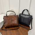 Brown and black leather handbags on a wooden surface with a white background