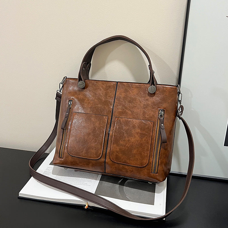 Brown leather handbag with a strap on a book against a neutral background