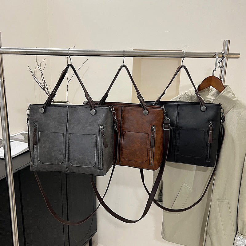 Three handbags in gray, brown, and black hanging on a rack.